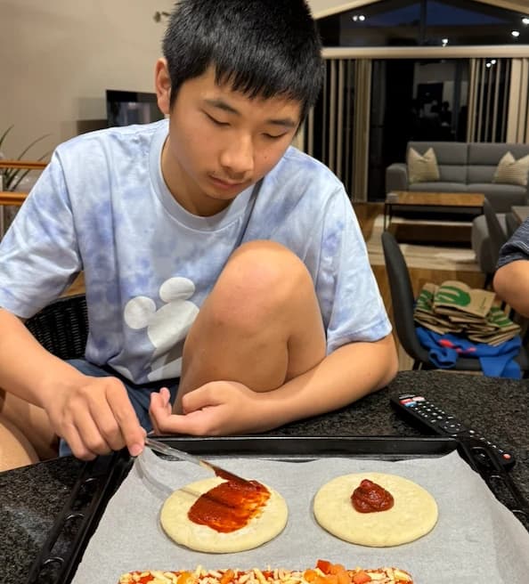 A participant spreading tomato sauce on pizza bases